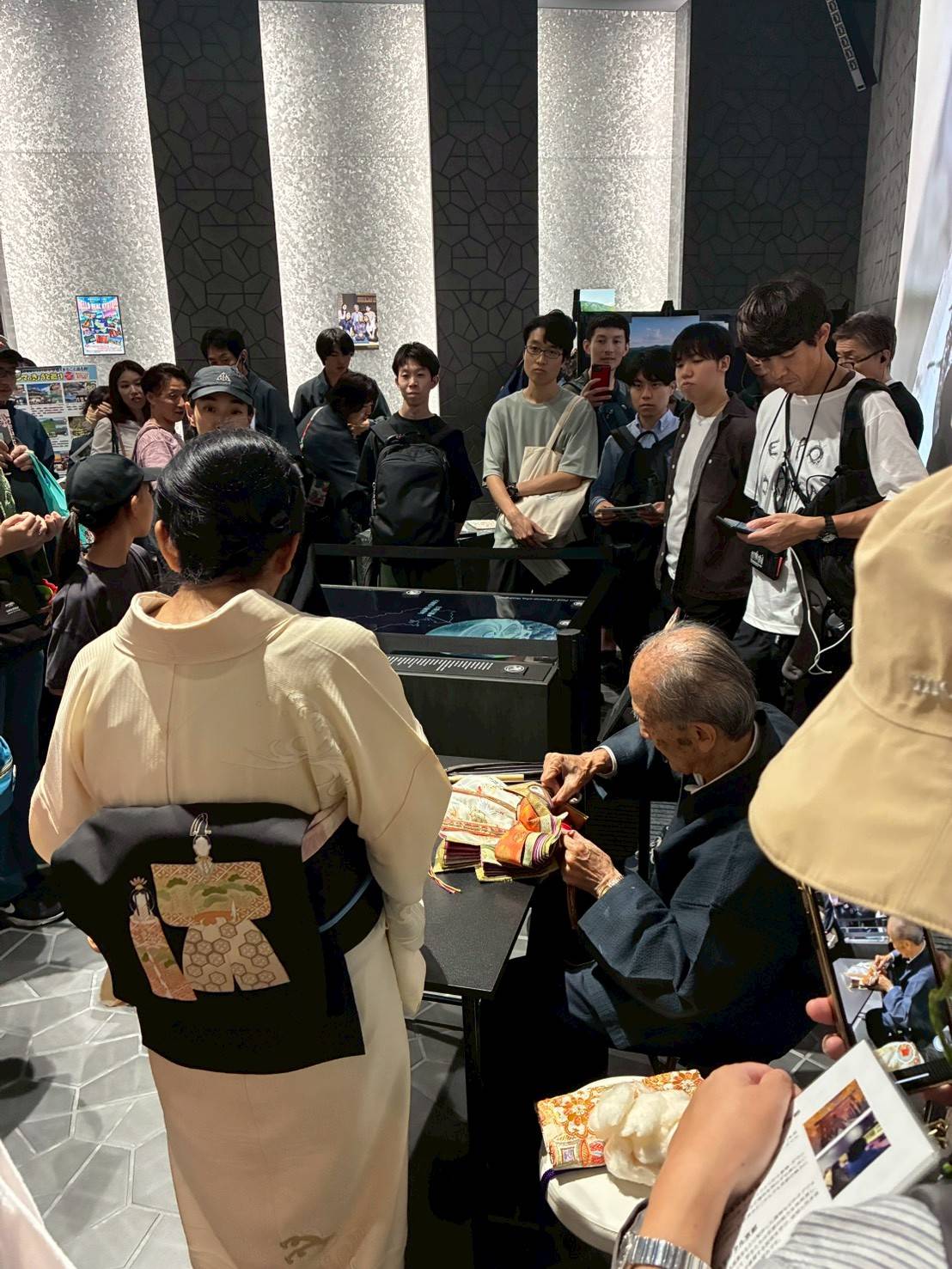 関西パビリオン京都ゾーンで雛人形の着付実演を行う三代目安藤桂甫と、見守る大勢の来場者